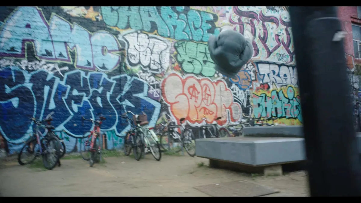 A person curled mid-air in a somersault above a concrete platform, bicycles parked against a graffiti-covered wall behind.