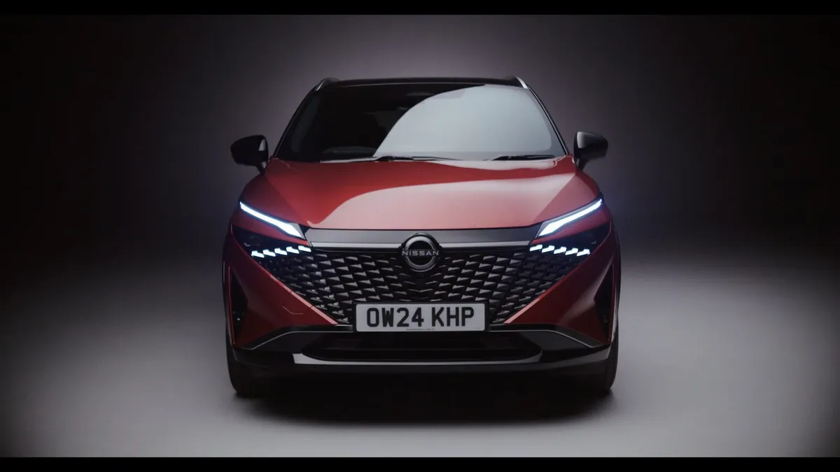 Front-on view of a red car with illuminated headlights and dark grille, lit against a dark studio background, registration plate OW24 KHP.