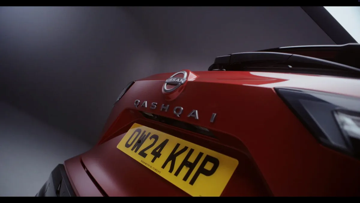 Close-up of the rear of a red Nissan Qashqai, showing badge and yellow number plate OW24 KHP, in a dark studio.