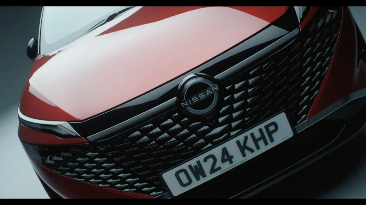 Close-up of a red car's bonnet and grille with Nissan badge and registration plate OW24 KHP, in a studio setting.