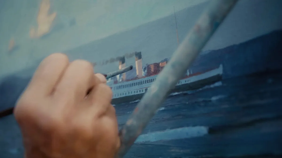 Close-up of a hand gripping a paintbrush against a wooden easel bar, painting a steamship on canvas.
