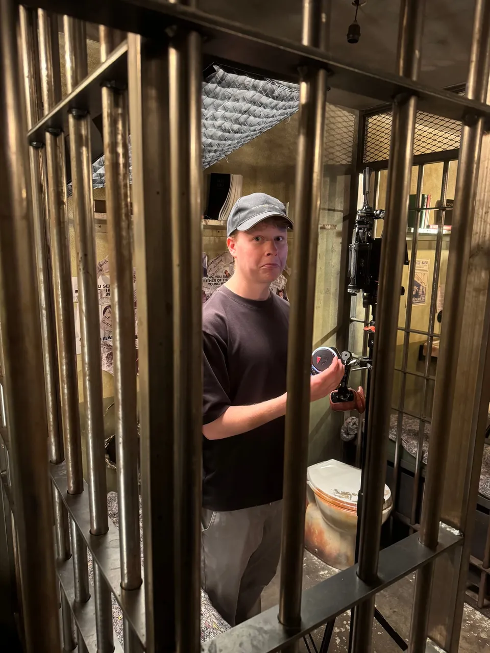 A focus puller in a cell, with a prop toilet and a light from the ceiling